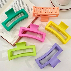 Set of six colorful 13cm matte square claw clips for thick hair arranged on an open book