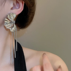 Close-up of silver metal flower earrings with long fringe tassels worn by a model