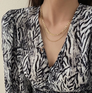 Close-up of layered gold figaro chain necklaces on a model in a deep V-neck dress