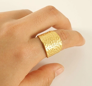 Close-up of golden wide-band ring with hammered texture worn on a finger