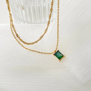Close-up of gold chain necklace featuring a rectangular emerald green gemstone pendant
