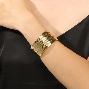 Detailed view of wide gold cuff bracelet featuring layered leaf texture on female wrist