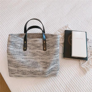 Détail d'un cabas en tweed tissé noir et blanc avec anses en cuir noir et rivets dorés