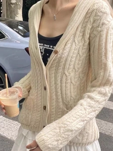 Outdoor shot of a woman wearing a cream cable knit button-up cardigan with V-neckline