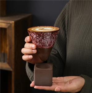 Close-up of rustic stoneware coffee mug with red glazed texture on a cubic brown base