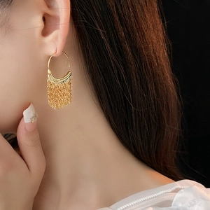 Close-up of elegant gold C-shaped tassel earrings worn by a model in soft lighting