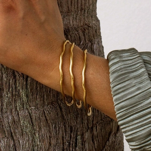 Detailed view of three-piece set golden wavy titanium steel bangles with polished finish