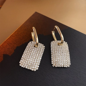 Vue macro de boucles d'oreilles rectangulaires dorées avec cristaux pavés sur bois