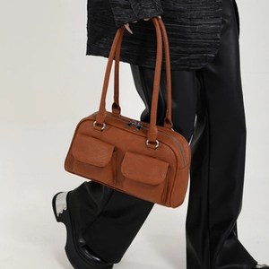 Side view of brown faux leather tote bag with dual front pockets on female model