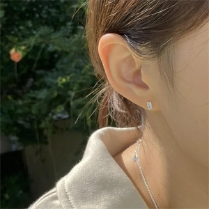 Close-up of minimalist rectangular crystal studs and heart pendant necklace on a model