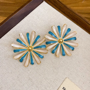 Vista macro degli orecchini a margherita blu e bianchi su espositore in lino beige