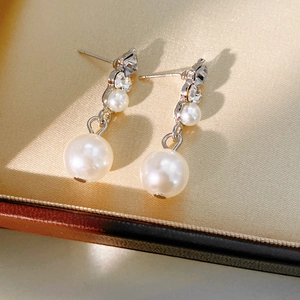 Close-up of elegant silver pearl earrings with crystals in a beige jewelry box