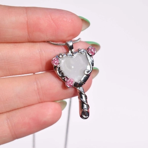Detailed close-up of silver heart mirror pendant with pink stones and white center stone