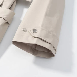 Detail of beige trench coat sleeve featuring adjustable straps and silver metal buttons