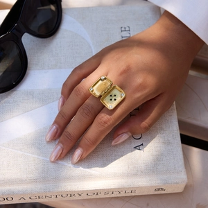 Detail of an openable 18K gold square locket ring worn on index finger over books