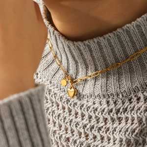 Collier à pendentif cœur en acier doré sur pull en maille grise, vue rapprochée