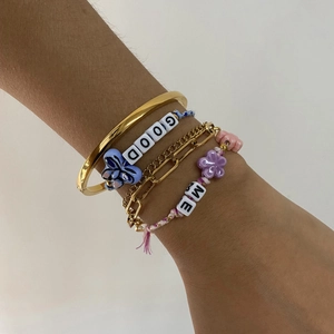 Macro shot of 4pcs layered bracelets with gold chain, colorful beads and flower charm