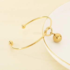 Detailed close-up of a polished gold open bangle featuring a hollow metal sphere charm
