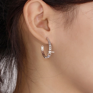 Macro shot of silver C-shaped hoop earring featuring hope letter and cuban chain texture