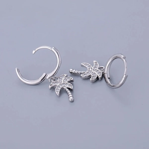 Close-up of silver hoop earrings with palm tree pendants and white zircon stones
