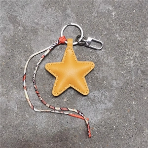 Close-up of yellow leather star keychain with metal clasp and printed silk scarf detail