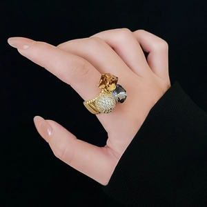 Macro detail of gold plated ring with square crystals and pavé sphere on black background