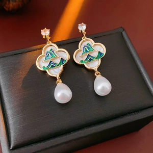 Détail de boucles d'oreilles dorées avec montagnes en émail vert et perle pendante