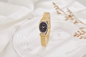 Close-up of elegant gold oval quartz watch with black dial and metal link strap
