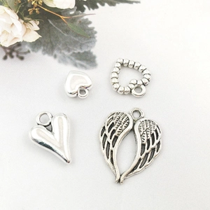 Macro view of silver hollow heart and angel wing alloy pendants on grey fabric background