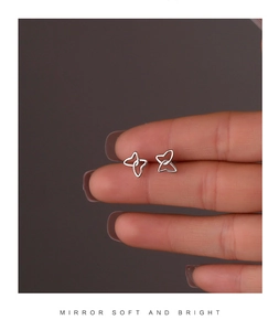 Macro shot of minimalist silver hollow butterfly stud earrings held to show mini size