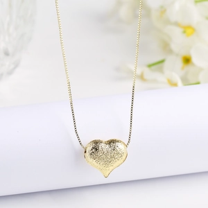 Detailed close-up of a matte gold heart pendant featuring a textured hammered finish on a box chain