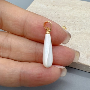 Detalle de colgante de nácar blanco en forma de gota con enganche dorado para joyas