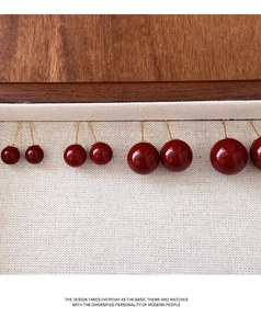 Detail view of four graduated red round ball stud earrings on beige canvas fabric