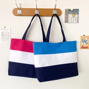 Detailed view of tricolor canvas tote bags hanging on wooden hooks against a white wall