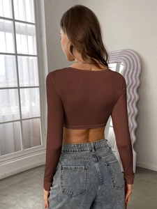 Rear view of model in brown cropped long sleeve top and denim jeans by a window
