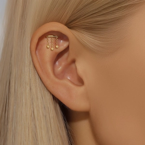 Close-up of golden minimalist ball tassel drop earring worn on the ear cartilage