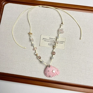 Detail of pink seashell pendant necklace with tiny pearls and star on woven cord