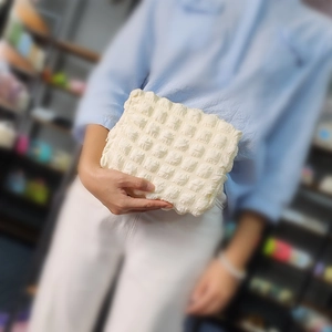 Detailed texture of cream bubble puff cosmetic bag held by a model for size