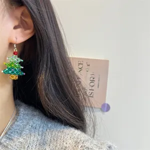 Close-up of handmade beaded Christmas tree earrings with colorful crystals on model