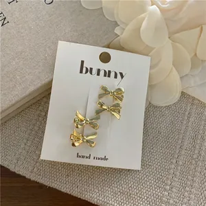 Set of four polished golden bow hair clips displayed on a white branded card