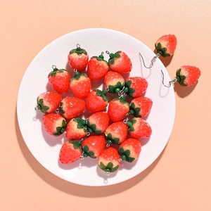 Close-up of resin strawberry charms and earrings on a plate for DIY jewelry making