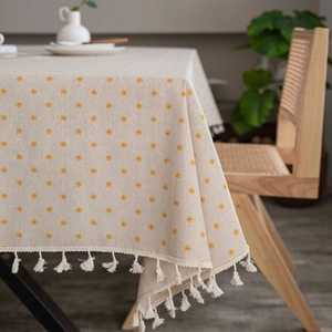 Detail of beige cotton linen tablecloth with yellow floral patterns and white fringe