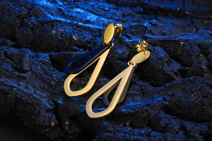 Close-up of gold and black double-layered teardrop earrings on a textured stone surface