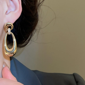 Close-up of gold-plated oval drop earrings with sparkling zircon accents on a model