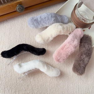 Detailed view of six fuzzy plush hair clips in neutral colors on beige fabric