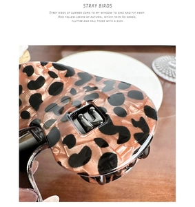 Macro shot of leopard print acetate hair claw clip featuring a metallic U-shaped emblem detail