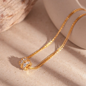Dettaglio macro di una collana dorata a doppio strato con pendente cilindrico di zirconi