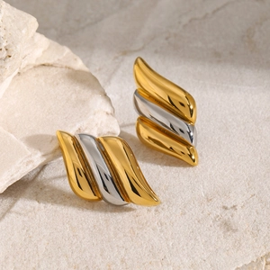 Close-up of wavy gold and silver two-tone earrings on a textured stone surface