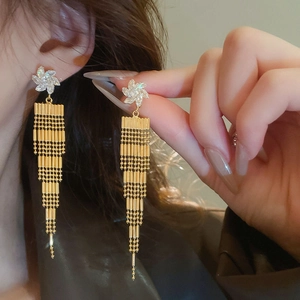 Close-up of model wearing gold long tassel earrings with white flower rhinestones