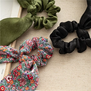Close-up of satin and floral scrunchies with long ribbons on a textured beige background